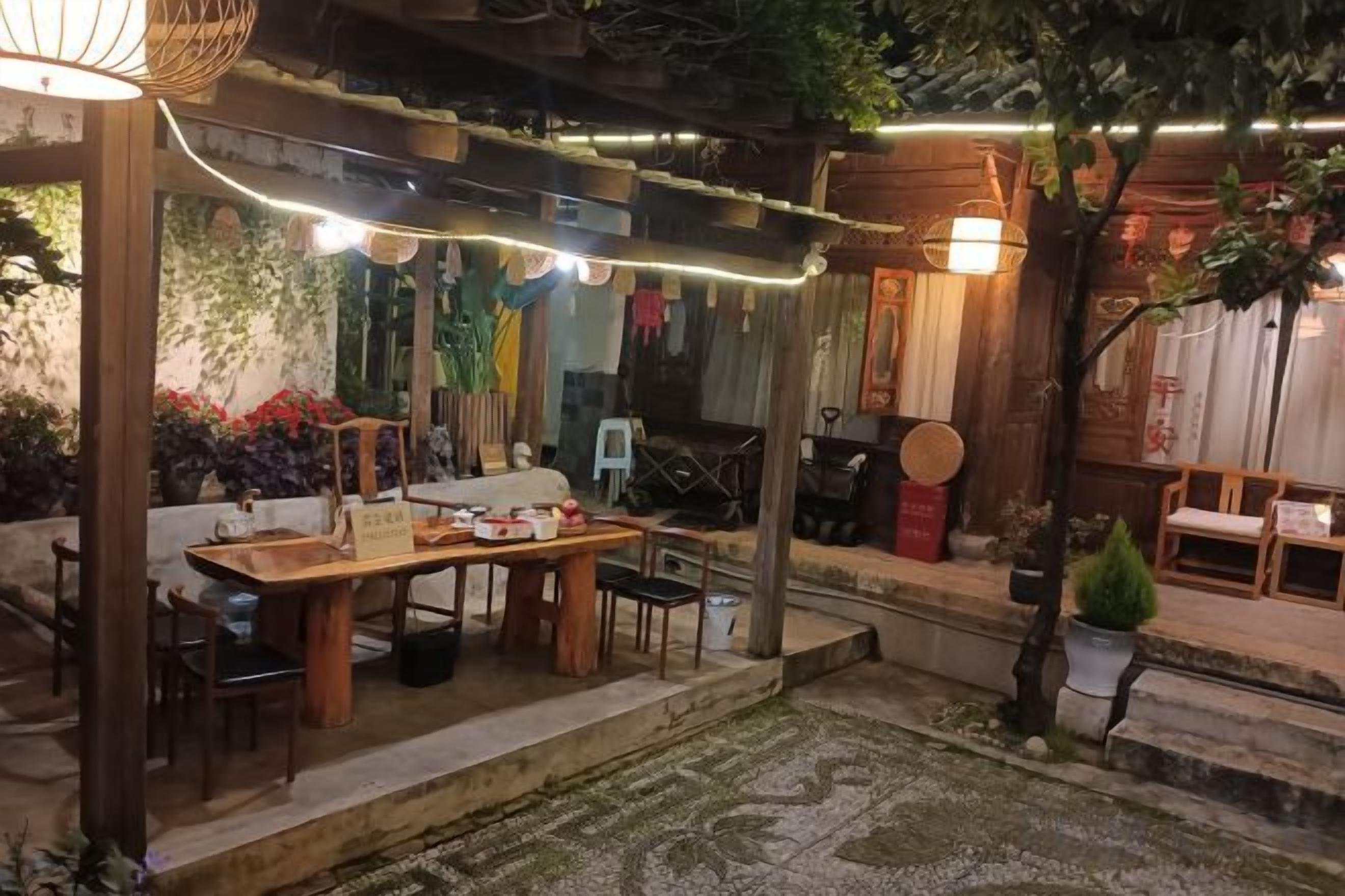An outdoor dining area with a wooden table and chairs, string lights, and potted plants.
