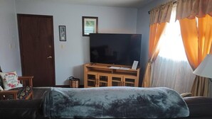 A living room with a dark sofa, a wooden entertainment unit with a TV, a door, and a window with curtains. - This apartment is a 1 bedroom(s), 1 bathrooms, located in Pierre, SD. (Pierre)