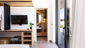 Ein modernes Schlafzimmer mit Bett, Schreibtisch und Fernseher. Es gibt ein Badezimmer mit Spiegel und Waschbecken. Der Raum hat ein großes Fenster und eine Schiebetür.