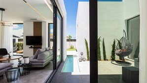Ein modernes Wohnzimmer mit einer Couch, einem Couchtisch und einem Fernseher. Es gibt einen kleinen Pool und Sitzgelegenheiten im Freien.