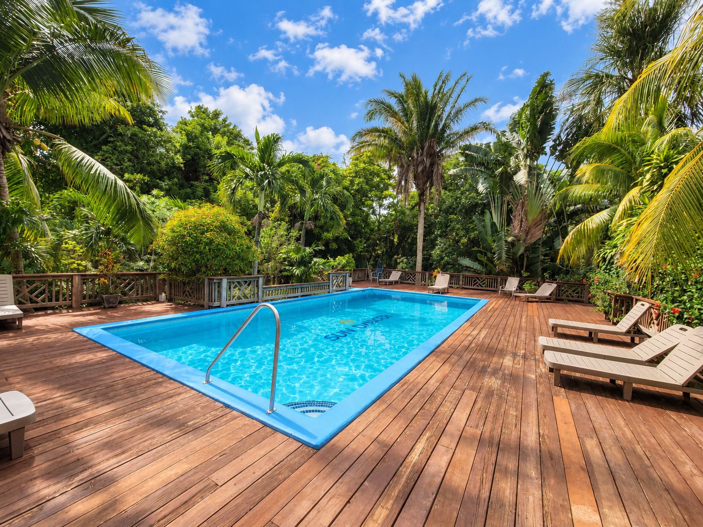 A wooden deck with a swimming pool, surrounded by lush greenery and palm trees.