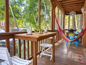 A wooden deck with a hammock, chairs, and a table with a cup and saucer.