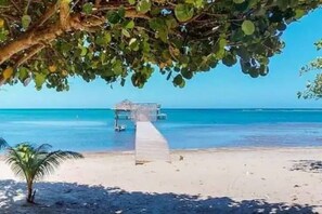 A beach with a wooden walkway leading to a structure by the water. - Casita de Nómadas - 2 Bedroom Beach House (Sandy Bay)