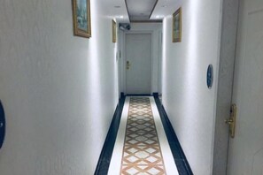 Ένας διάδρομος με ένα διακοσμητικό δάπεδο, μια πόρτα στο τέλος και ένας διακόπτης φωτός στον τοίχο.