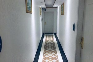 Un pasillo con piso estampado, una puerta al final y un interruptor de luz en la pared.
