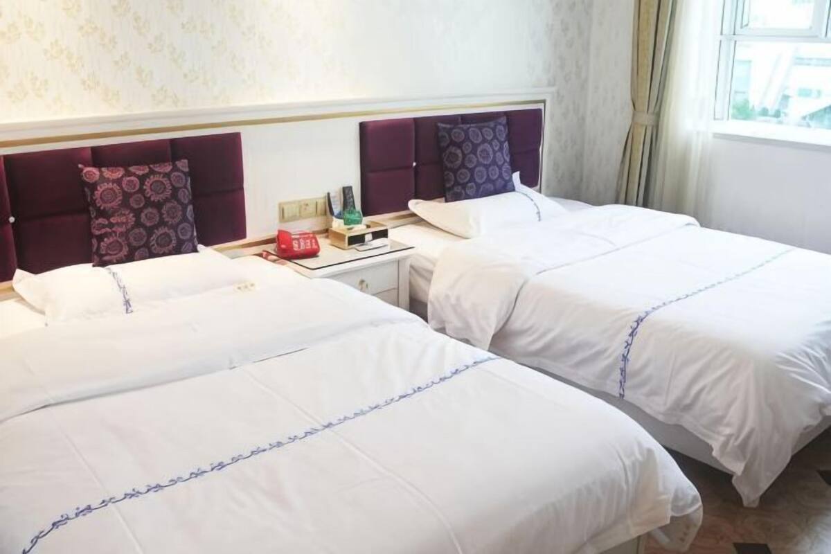 A hotel room with two beds, a nightstand with a lamp, and a window with curtains.