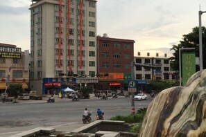 Un edificio de varios pisos con comercios en la planta baja, una intersección de tráfico y una fuente en primer plano.