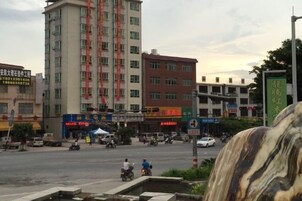 Un edificio de varios pisos con comercios en la planta baja, una intersección de tráfico y una fuente en primer plano.