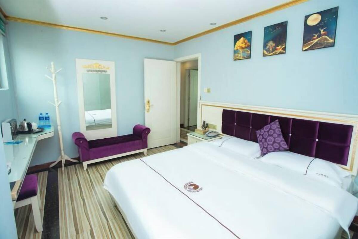 A hotel room with a bed, a desk, a chair, a mirror, and artwork on the wall.