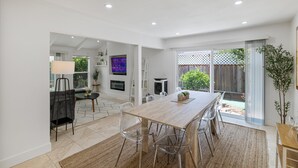 Une cuisine moderne avec une table à manger en bois, des chaises transparentes et un téléviseur fixé au mur.