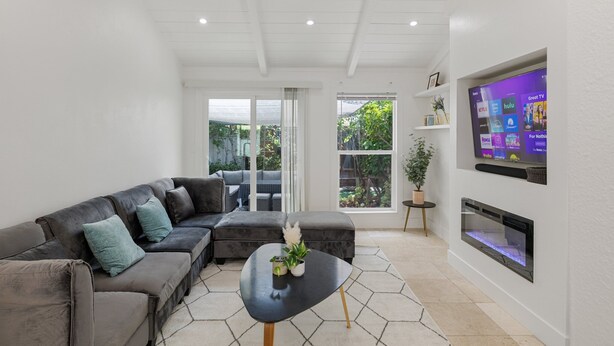 Un salon moderne avec un canapé d’angle, une table basse noire et un téléviseur à écran plat fixé au mur.