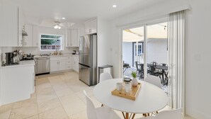 Une cuisine moderne avec des meubles blancs, un réfrigérateur en acier inoxydable et un coin repas comprenant une table et des chaises blanches.