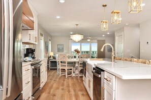 A modern kitchen with white cabinetry, a central island, and a dining area with wooden chairs and a table. - Sea Cliff K68 - Aqua La Vista Baby! (Port St. Joe)