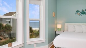 Ein Schlafzimmer mit Blick auf den Strand, ein Bett, ein Nachttisch mit Lampe und ein Schild mit der Aufschrift 'No Wake Zone' am Fenster.