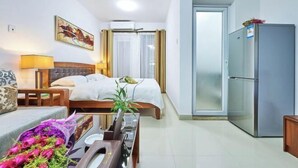 A hotel room with a bed, a desk, a chair, a lamp, a refrigerator, and a window with curtains. - Shanghe Apartment (Shenzhen Science and Technology Park MixC World) (Shenzhen)