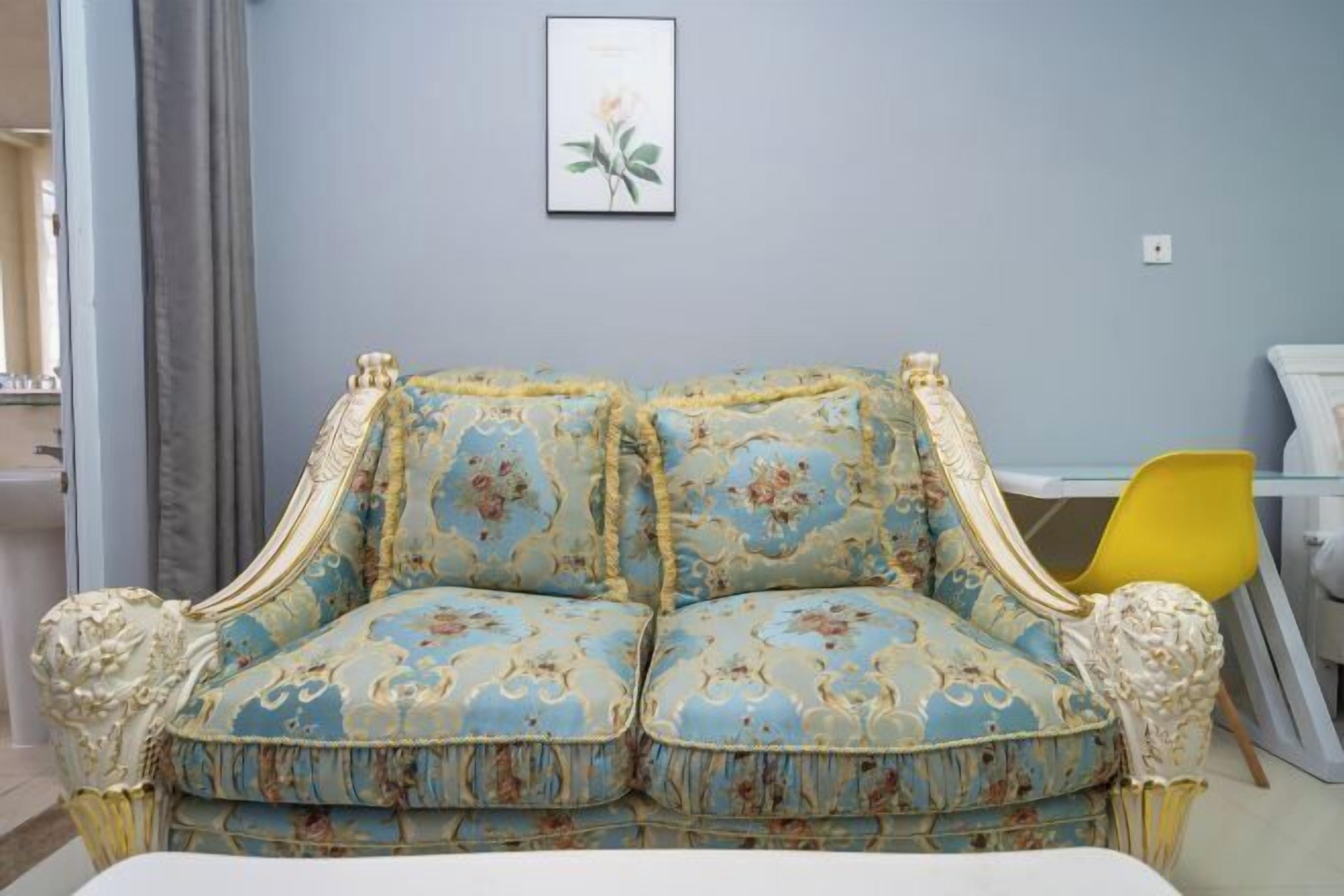 A room with a blue floral sofa, a yellow chair, and a framed picture on the wall.