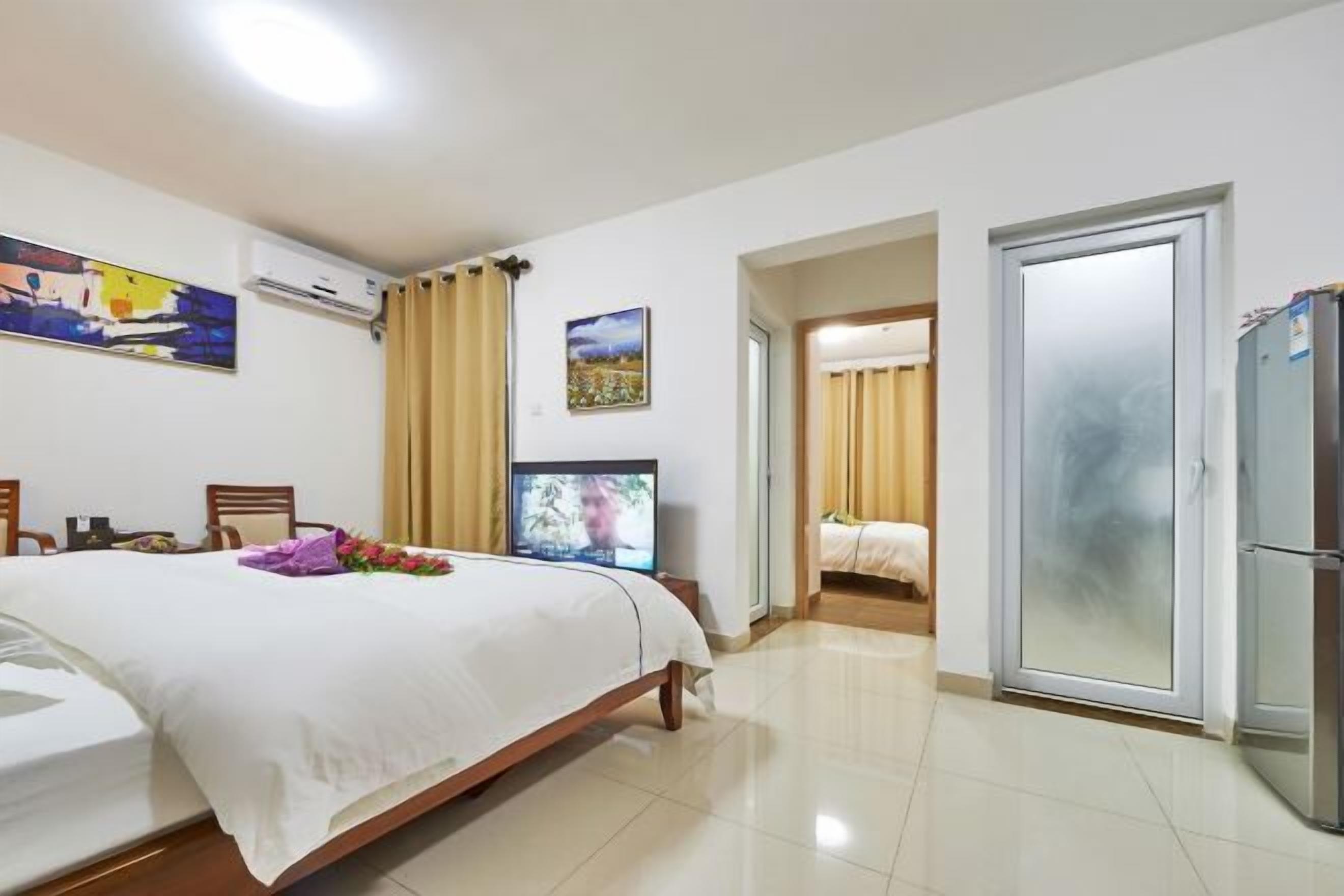 A hotel room with a bed, a television, a refrigerator, and a door leading to another room.