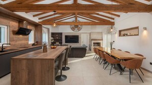 A modern kitchen with wooden beams, a central island, and a dining area with a long table and chairs. - Villa Unika heated Pool, Jacuzzi, Sauna (Opanci)