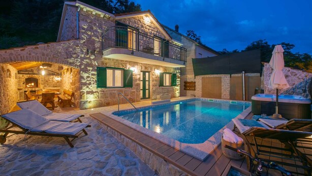 Een stenen villa met zwembad, buitenterras en een hottub.