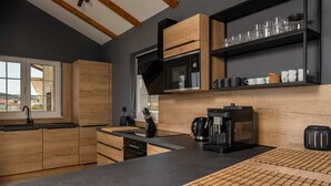 Une cuisine moderne avec des meubles en bois, un plan de travail noir, une machine à café et une fenêtre donnant sur des maisons.