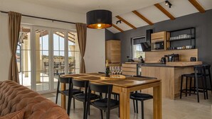 Une cuisine moderne avec un îlot central en bois, un coin repas avec une table et des chaises, et une vue à travers les portes vitrées.