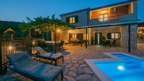 A two-story house with a pool, outdoor seating, and a stone patio.