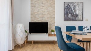 A modern living room with a flat-screen TV, a dining area with blue chairs, and a stone-patterned wall.