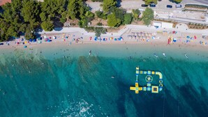 Vue aérienne d’une plage aux eaux cristallines, avec une jetée et des parasols de plage.