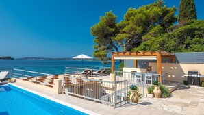 Un espace piscine avec des chaises longues, une pergola et une vue sur la mer.