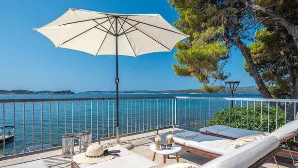 Un balcon équipé de chaises longues, d’une table et d’un parasol, donnant sur une étendue d’eau.