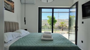 Ein Schlafzimmer mit einem Bett, Blick durch eine Glastür und einem Wand-Fernseher.