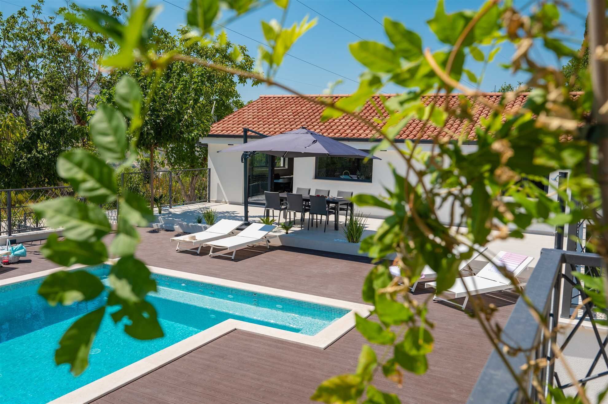 A modern outdoor pool area with lounge chairs, a dining set, and a covered patio.