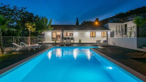 Ein modernes Haus mit Swimmingpool, Sitzgelegenheit im Freien und einer gut beleuchteten Terrassenfläche.