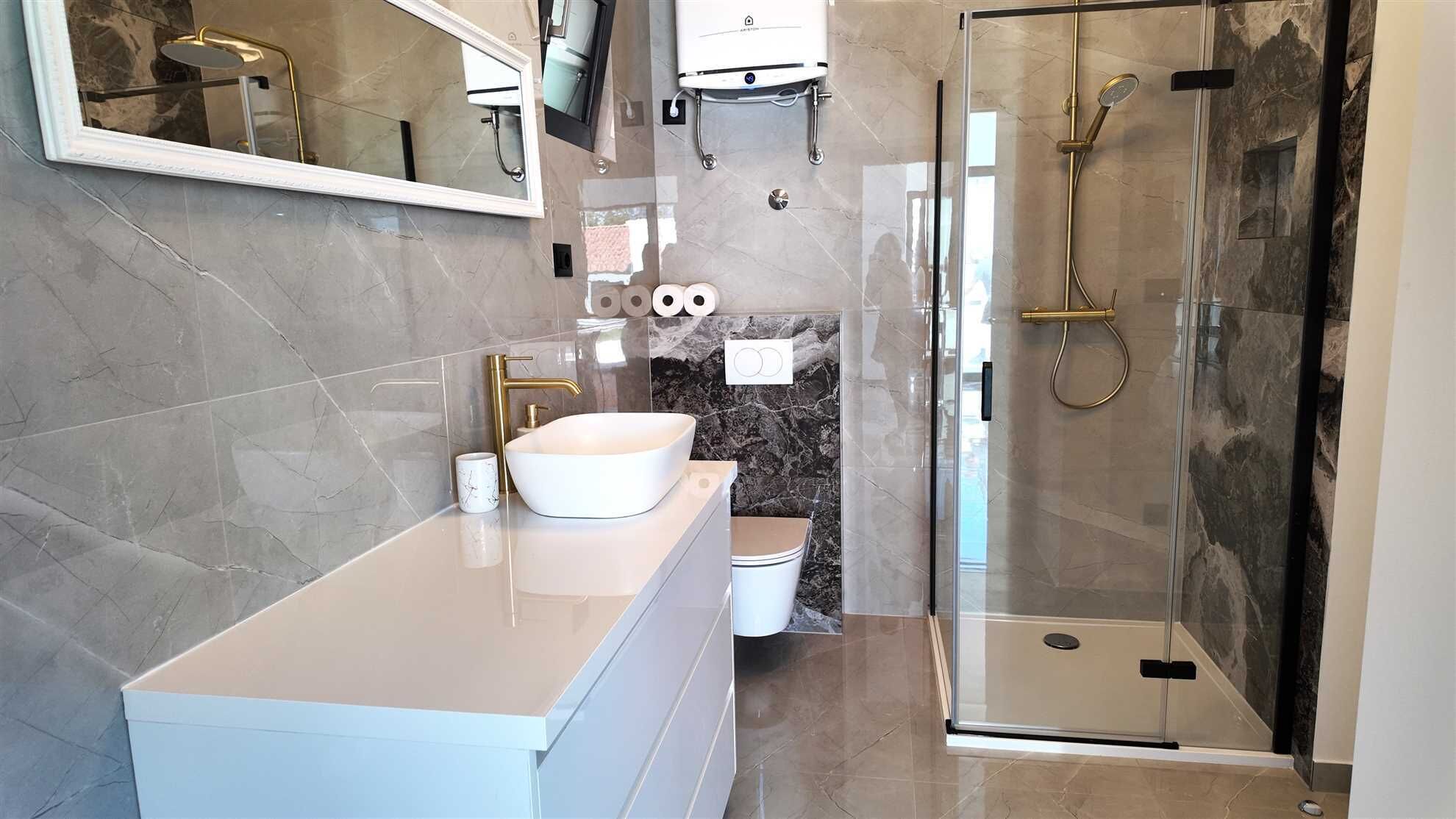 Ein modernes Badezimmer mit großem Spiegel, weißem Waschbecken, einer Dusche mit Glasabtrennung und Marmorwänden.
