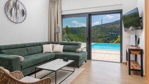 A modern living room with a green sofa, a coffee table, and a TV on a wooden stand. - Villa Nacle with heated Pool near Omiš (Tugare)