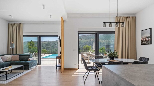 A modern living room with a pool view, a dining area, and a large sliding glass door leading to a balcony. - Villa Nacle with heated Pool near Omiš (Tugare)