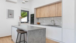 A modern kitchen with a large island, wooden cabinets, a marble backsplash, and a window with a view of greenery. - Villa Nacle with heated Pool near Omiš (Tugare)