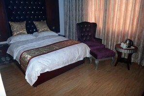 A double bed with a headboard, a chair, a small round table with a kettle, and curtains. - Jinchuan Noah Ark Hotel (Jinchuan)