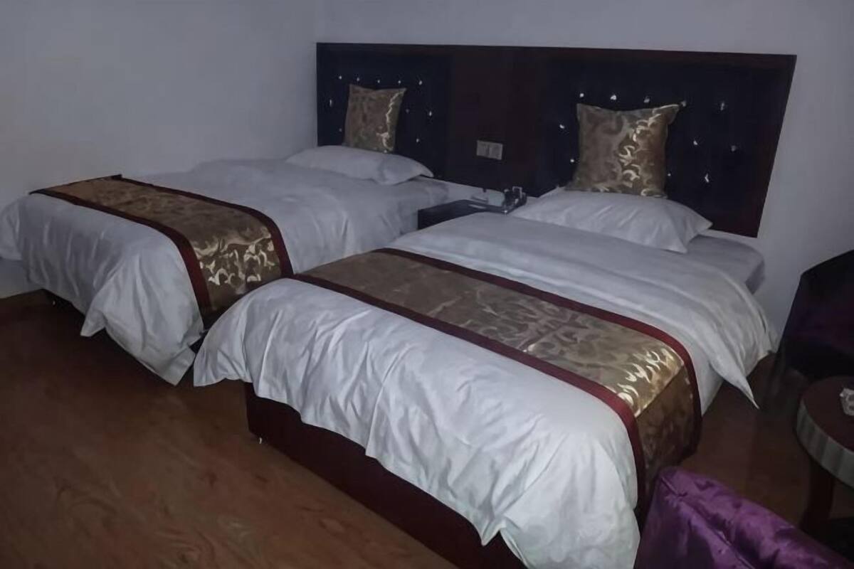 A hotel room with two beds, wooden flooring, and a dark headboard.