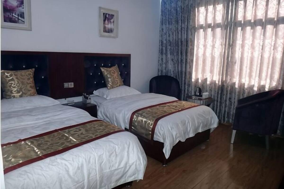 A hotel room with two beds, a nightstand, a chair, and a large window with curtains.