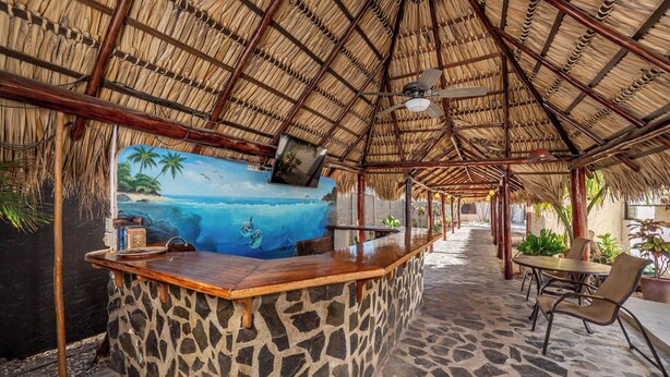 A tiki bar with a stone counter, a mural of a beach scene, and a thatched roof.