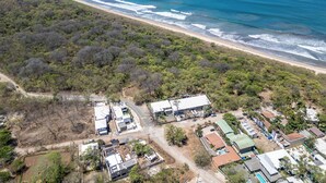 An aerial view of a coastal area with a beach, dense vegetation, and a mix of residential and commercial buildings.