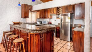 A kitchen with wooden cabinets, a granite countertop, a stainless steel refrigerator, and a blue pendant light.