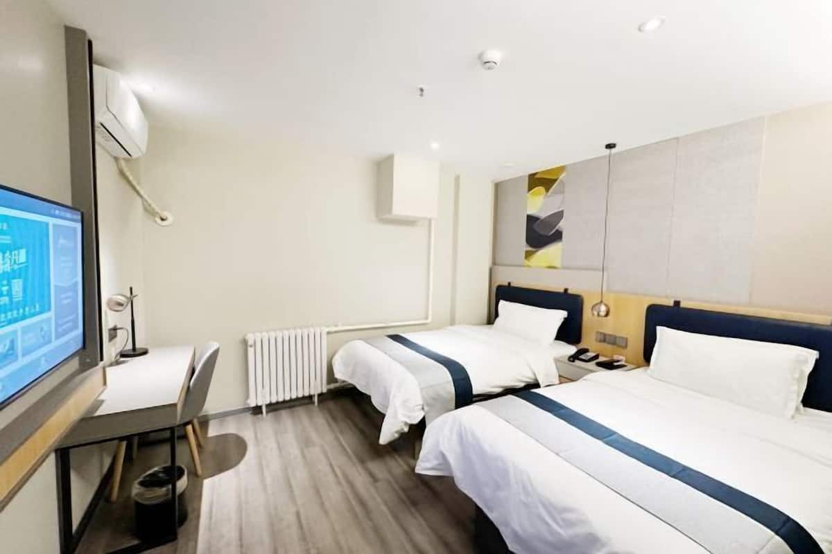 Une chambre d’hôtel avec deux lits, un bureau, une chaise, un téléviseur et un radiateur.