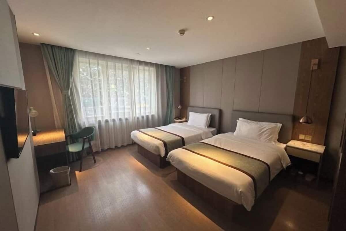 Une chambre d’hôtel avec deux lits, un bureau, une chaise, une fenêtre avec des rideaux et un téléviseur.