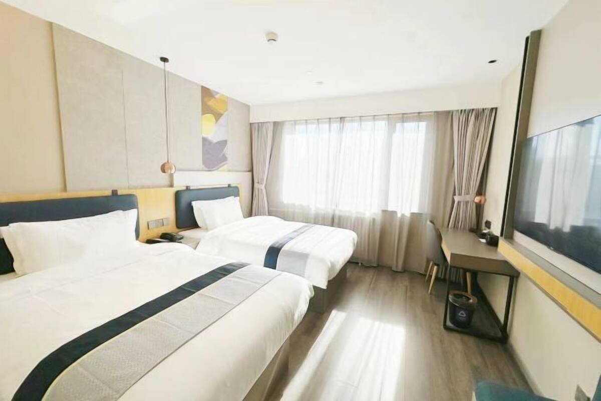 Une chambre d’hôtel avec deux lits, un bureau, une chaise et une grande fenêtre avec des rideaux.
