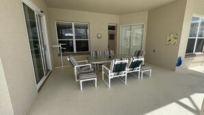 Un patio cubierto con mesa y sillas, ventanas grandes y un reloj en la pared.