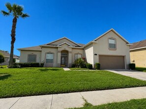 A two-story house with a front garage, a well-maintained lawn, and a palm tree.