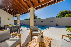 A covered outdoor area with a pool, wooden furniture, and a table with a bottle of champagne.