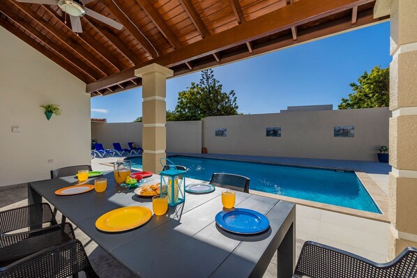An outdoor dining area with a pool view, featuring a table set with plates, glasses, and a lantern. - Spacious Renovated House Prvt Pool 5 min to Bch (Noord)
